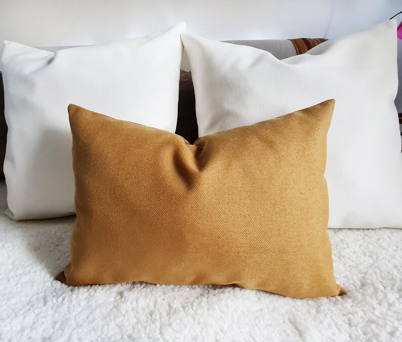 May include: Three throw pillows, one mustard yellow and two white, arranged on a white fluffy surface.