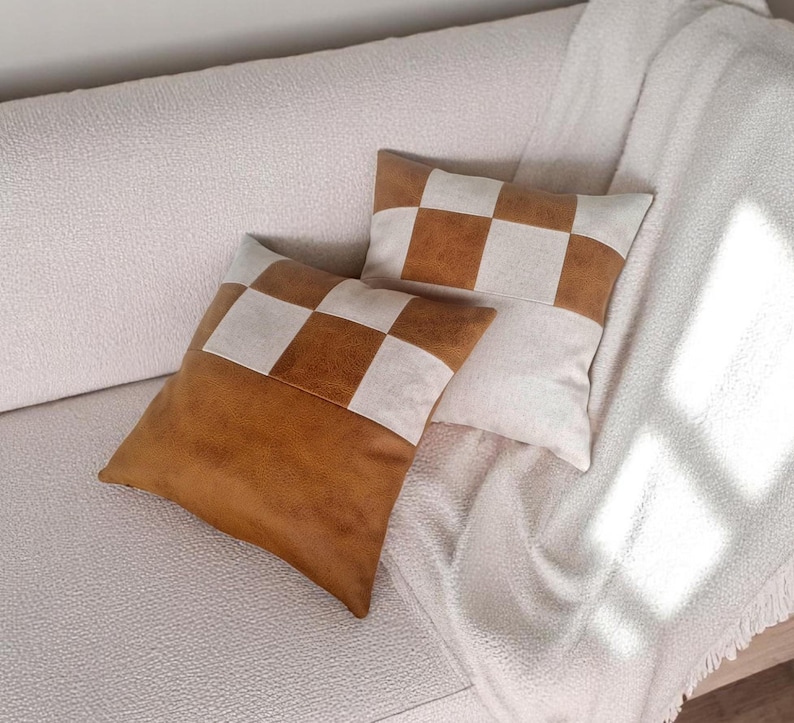 May include: Two decorative throw pillows with a checkered pattern. The pillows are made of a brown faux leather and white fabric. The pillows are on a white couch.