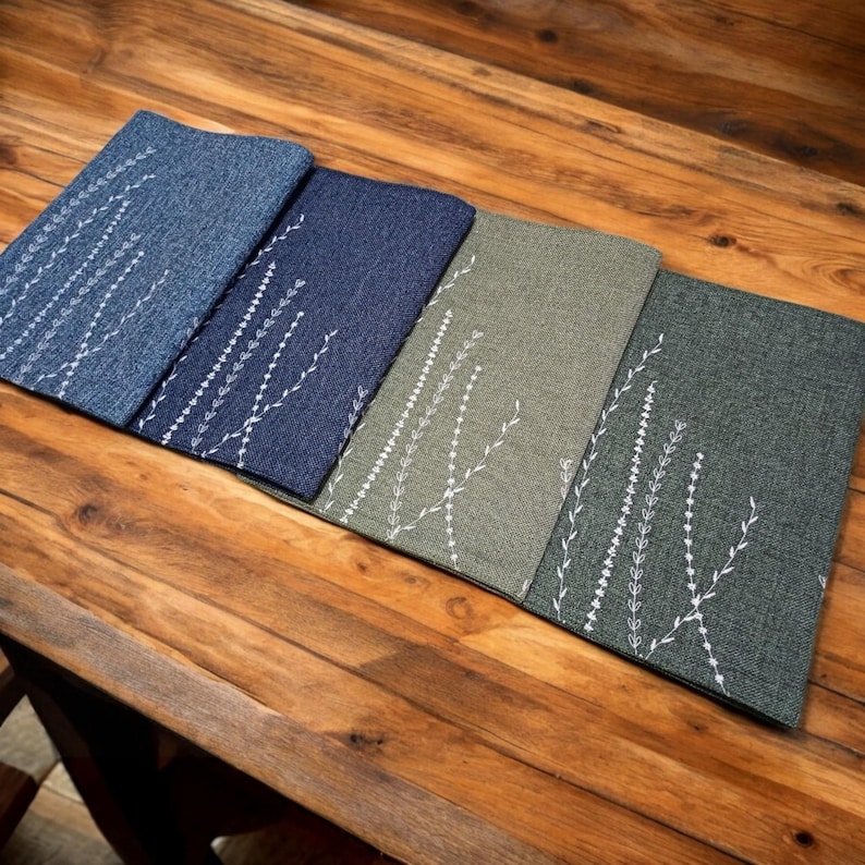 May include: Four placemats with a white embroidered floral design. The placemats are in shades of blue and green.