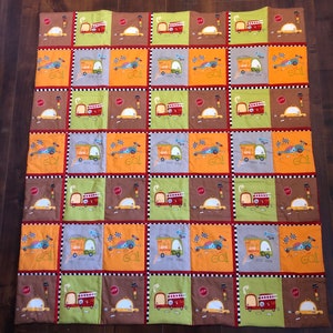 May include: A colourful patchwork quilt with a repeating pattern of toy trucks, cars, and traffic lights. The quilt is made of various fabrics in shades of brown, green, yellow, orange, and red.