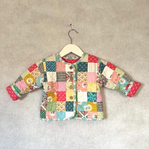 May include: A patchwork jacket in a variety of colours, including pink, green, blue, and yellow. The jacket features a round collar, long sleeves, and is fastened with three wooden buttons. The trim is red.