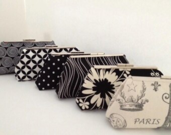 May include: A set of seven black and white fabric clutches with different patterns. The clutches have silver clasps and are arranged in a row from largest to smallest.