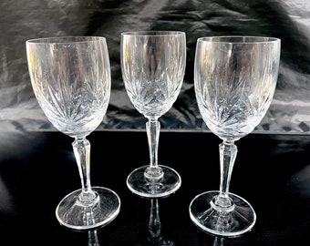 May include: Three clear glass wine glasses with a cut crystal design. The glasses are on a black surface.
