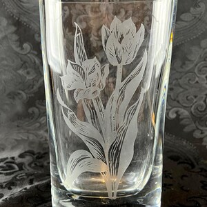 Op de afbeelding: Een helder drinkglas met een mat, ge&euml;tst ontwerp van twee tulpen met lange stelen en bladeren. Het glas heeft een gladde, cilindrische vorm met een dikke bodem en toont een gedetailleerde botanische illustratie in een matte witte afwerking.