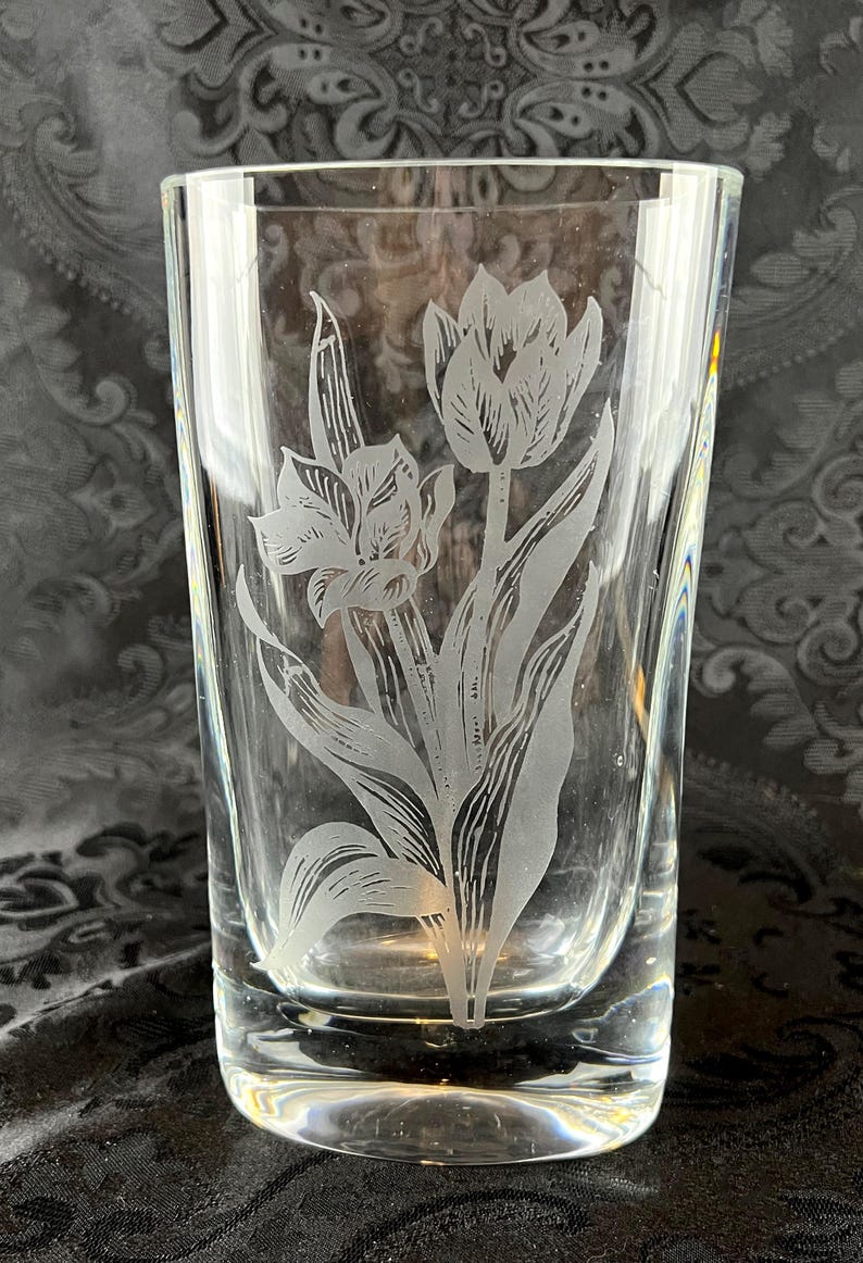 Op de afbeelding: Een helder drinkglas met een mat, ge&euml;tst ontwerp van twee tulpen met lange stelen en bladeren. Het glas heeft een gladde, cilindrische vorm met een dikke bodem en toont een gedetailleerde botanische illustratie in een matte witte afwerking.