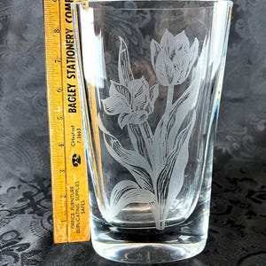 Op de afbeelding: Een heldere glazen vaas met een ge&euml;tst bloemmotief van tulpen en bladeren. Een gele houten liniaal is verticaal naast de vaas geplaatst en toont een hoogte van ongeveer 25,4 cm vanaf de basis tot aan de bovenrand van het glas.