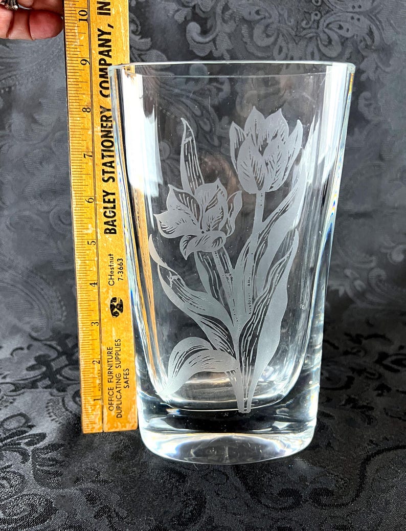 Op de afbeelding: Een heldere glazen vaas met een ge&euml;tst bloemmotief van tulpen en bladeren. Een gele houten liniaal is verticaal naast de vaas geplaatst en toont een hoogte van ongeveer 25,4 cm vanaf de basis tot aan de bovenrand van het glas.