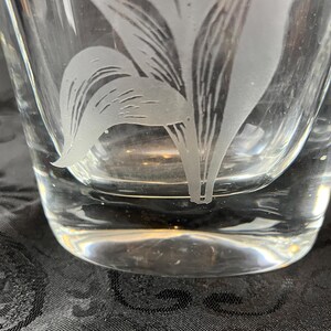 Op de afbeelding: Een helder glazen vat met een mat, ge&euml;tst ontwerp van een botanische plant met langwerpige bladeren. Het glas heeft een glad, transparant oppervlak met een dikke bodem, waarop het ingewikkelde, mat getextureerde bloemmotief direct is ge&euml;tst.