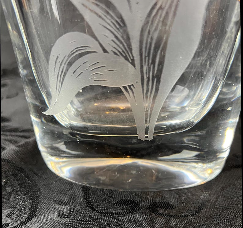 Op de afbeelding: Een helder glazen vat met een mat, ge&euml;tst ontwerp van een botanische plant met langwerpige bladeren. Het glas heeft een glad, transparant oppervlak met een dikke bodem, waarop het ingewikkelde, mat getextureerde bloemmotief direct is ge&euml;tst.