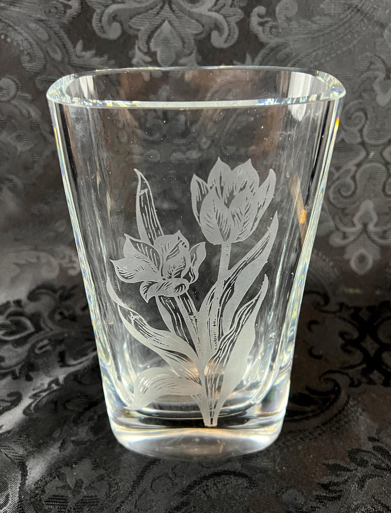 Op de afbeelding: Een heldere glazen vaas met een ge&euml;tst ontwerp van twee tulpen met gedetailleerde bloemblaadjes en bladeren. De vaas heeft een taps toelopende, cilindrische vorm met een dikke, massieve voet en gladde, transparante wanden met een gravure.