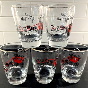 May include: Set of five vintage clear glass tumblers with a black and red stagecoach design. The glasses have a gold rim and a black base. The design features a horse-drawn carriage and buildings.