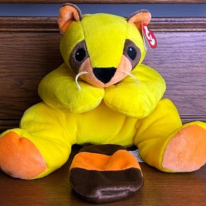 May include: Yellow plush raccoon with a brown and orange striped tail. The raccoon has a brown nose, black eyes, and orange accents on its paws.