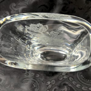 Op de afbeelding: Een heldere glazen kom met een ovale vorm en dikke wanden. De binnenkant van de bodem is voorzien van een ge&euml;tst ontwerp van twee bloeiende tulpen met gedetailleerde bloemblaadjes en bladeren. Het glas is transparant, glad en reflecteert licht.