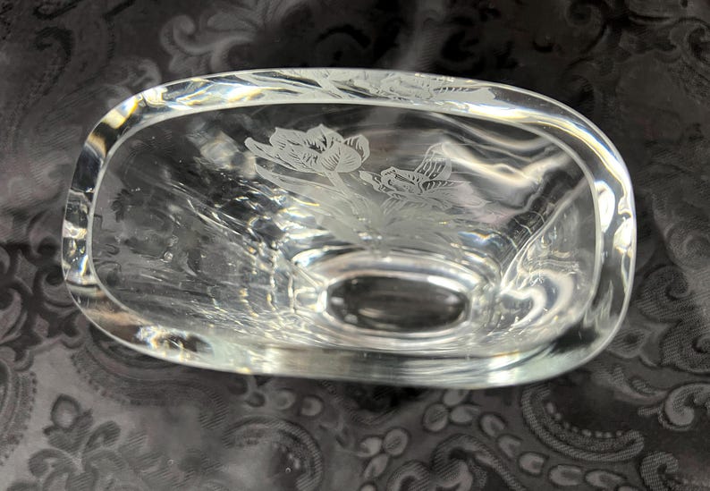 Op de afbeelding: Een heldere glazen kom met een ovale vorm en dikke wanden. De binnenkant van de bodem is voorzien van een ge&euml;tst ontwerp van twee bloeiende tulpen met gedetailleerde bloemblaadjes en bladeren. Het glas is transparant, glad en reflecteert licht.