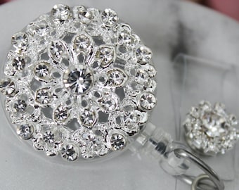 May include: A silver retractable badge reel with a sparkling, round, rhinestone design. A smaller, matching rhinestone accent is also included. The reel has a clear plastic backing and a metal clip for attachment.