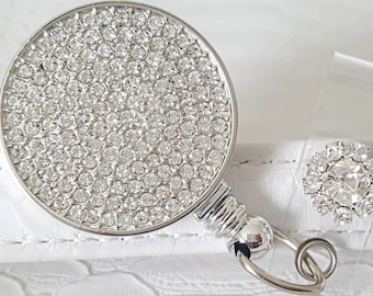May include: A silver retractable badge holder with a round, clear crystal-covered face and a matching crystal-covered clip.