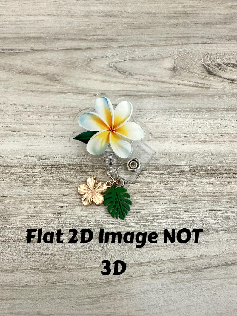 K&ouml;nnte beinhalten: Ein durchsichtiges Ausweis-Jojo mit einem Design einer wei&szlig;en und gelben Plumeria-Blume mit einem gr&uuml;nen Blatt. Ein goldener Blumen- und gr&uuml;ner Blatt-Anh&auml;nger h&auml;ngt darunter. Der Text "Flat 2D Image NOT 3D" ist in Schwarz gedruckt.