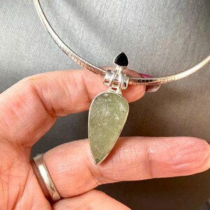 May include: A silver chain necklace with a pendant featuring a light green stone and a black gemstone. The pendant is shaped like a teardrop.
