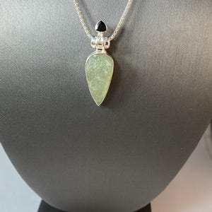 May include: A silver chain necklace with a green gemstone pendant and a black gemstone accent.