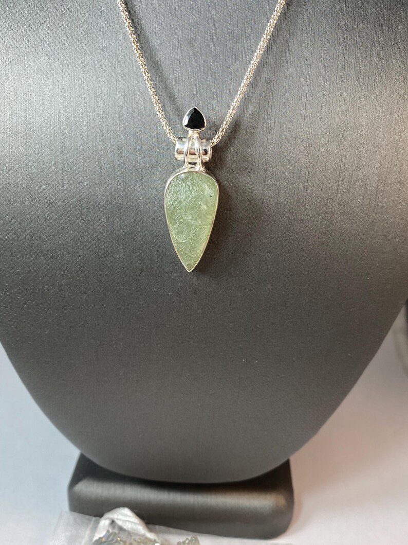 May include: A silver chain necklace with a green gemstone pendant and a black gemstone accent.