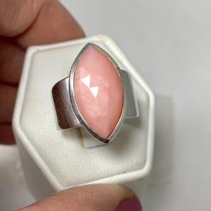 Pode incluir: Um anel de prata com uma gema de opala rosa em forma de marquise. O anel est&aacute; em uma caixa de exibi&ccedil;&atilde;o de anel branca.