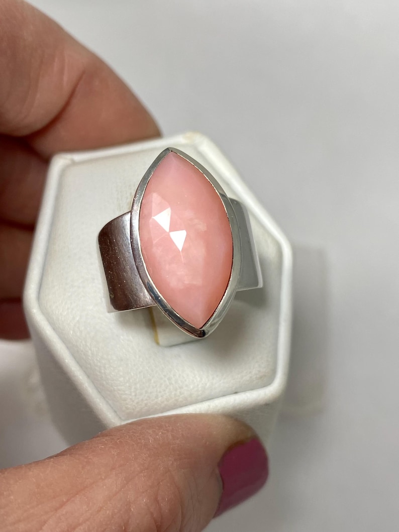 Pode incluir: Um anel de prata com uma gema de opala rosa em forma de marquise. O anel est&aacute; em uma caixa de exibi&ccedil;&atilde;o de anel branca.