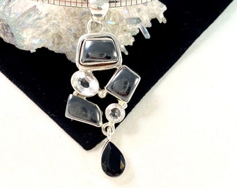 May include: A silver chain necklace with a pendant featuring a cluster of black and clear gemstones. The pendant is shaped like a teardrop with a smaller teardrop hanging from the bottom.