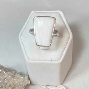May include: A white gemstone ring with a silver band. The gemstone is a rectangular shape with rounded corners and a textured surface.