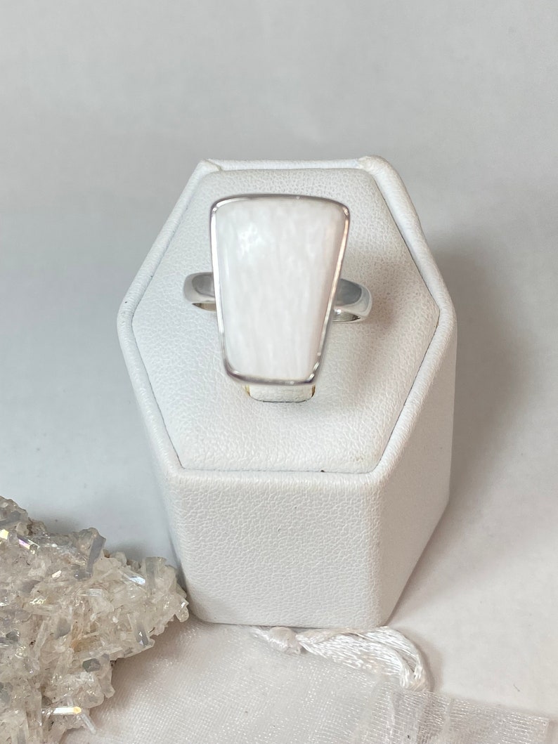 May include: A white gemstone ring with a silver band. The gemstone is a rectangular shape with rounded corners and a textured surface.