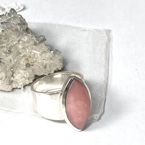 Pode incluir: Um anel de prata com uma gema rosa em forma de marquise. O anel est&aacute; sobre um fundo branco.