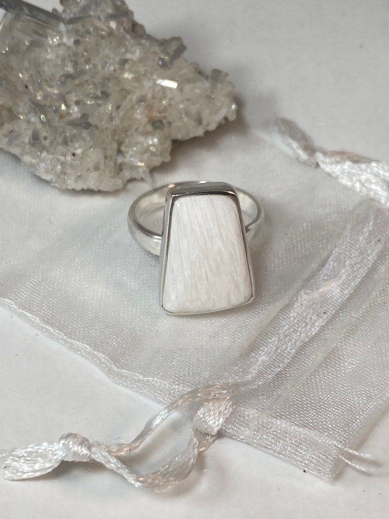 May include: A white rectangular ring with a silver band. The ring is made of a white stone with a textured surface.