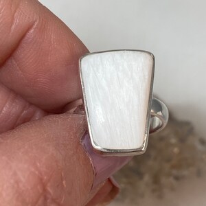 May include: A white gemstone ring with a silver band. The gemstone is a rectangular shape with rounded corners and has a striated texture.