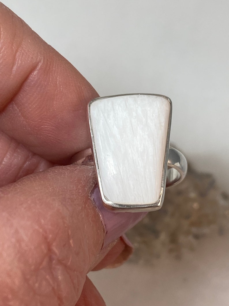 May include: A white gemstone ring with a silver band. The gemstone is a rectangular shape with rounded corners and has a striated texture.