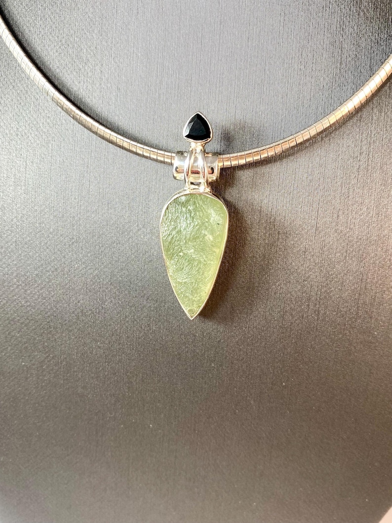 May include: A silver chain necklace with a pendant featuring a green gemstone and a black gemstone. The pendant is shaped like a teardrop.