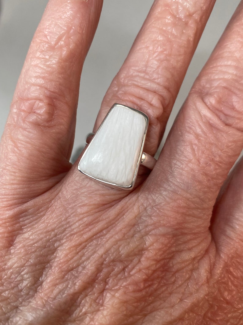 May include: A white ring with a rectangular shaped stone. The stone has a striated pattern.