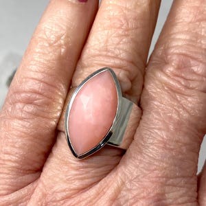 Pode incluir: Um anel de prata com uma grande gema rosa em forma de marquise. O anel &eacute; usado em um dedo.