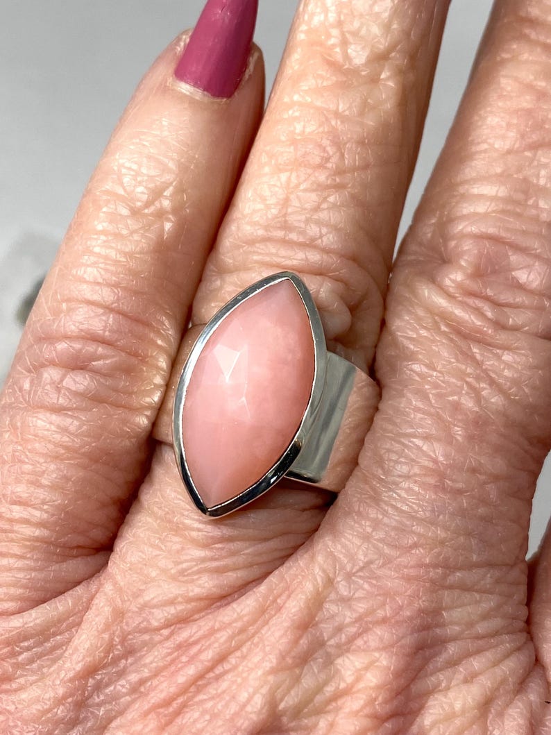 Pode incluir: Um anel de prata com uma grande gema rosa em forma de marquise. O anel &eacute; usado em um dedo.