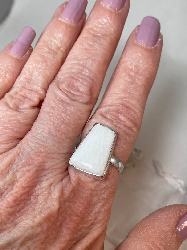 May include: A white, rectangular ring with a silver band. The ring is made of a white, striated material.