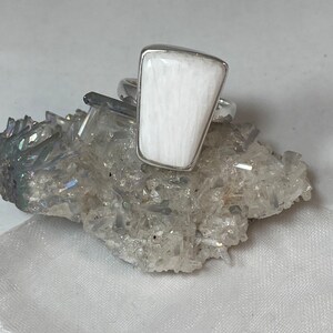 May include: A white selenite ring with a silver band. The ring is set on a bed of clear quartz crystals.