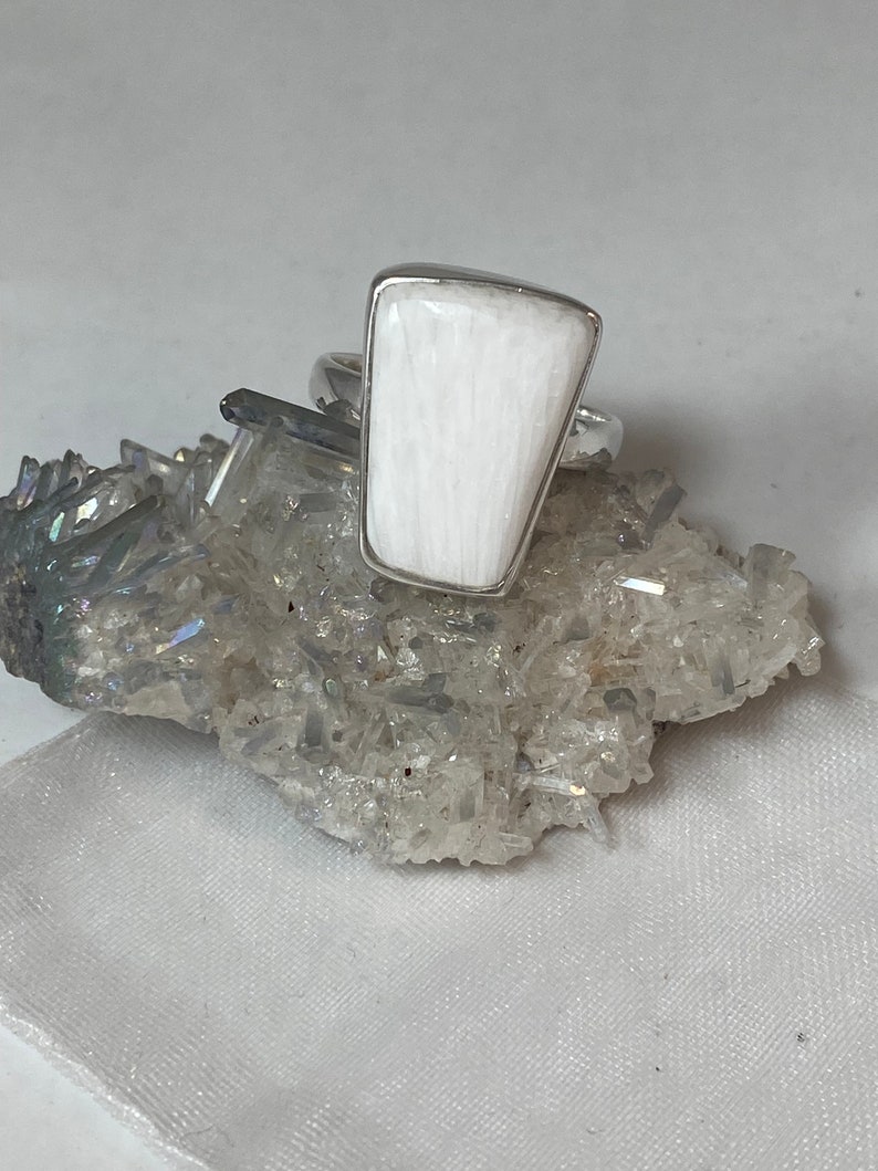 May include: A white selenite ring with a silver band. The ring is set on a bed of clear quartz crystals.