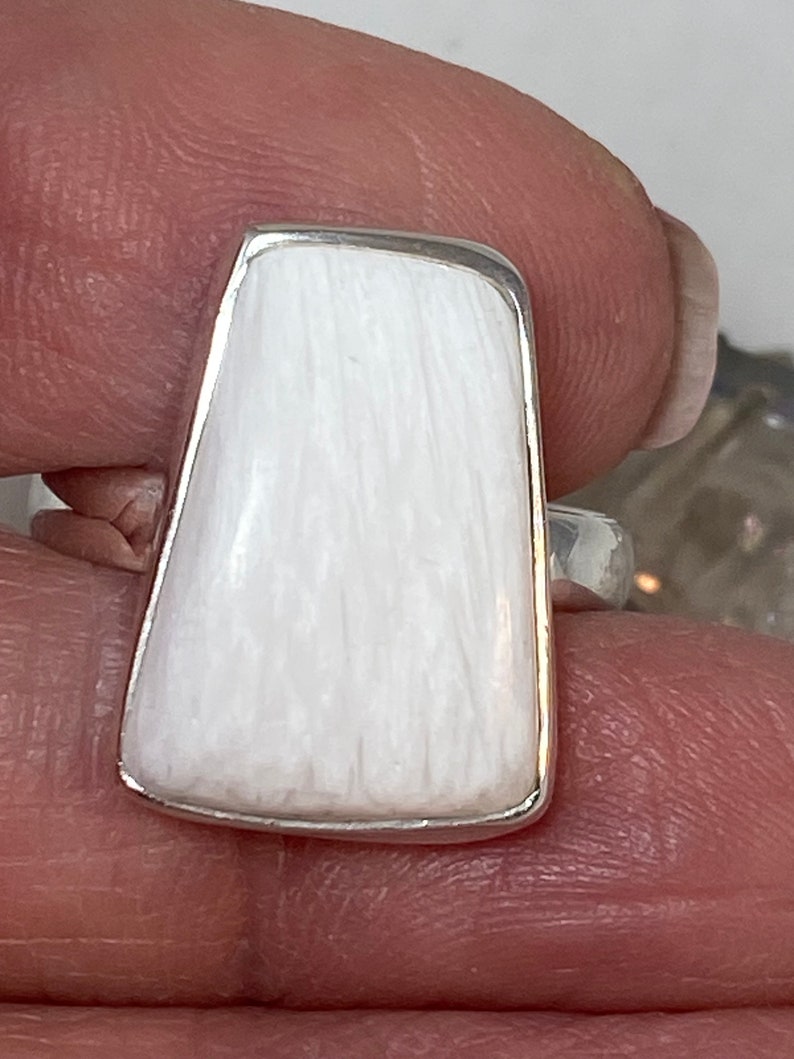 May include: A white rectangular ring with a silver band. The ring is made of a smooth, white material with a textured surface.