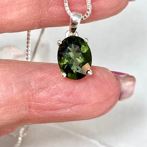 May include: A silver chain necklace with a green gemstone pendant. The gemstone is oval shaped and has a faceted cut.