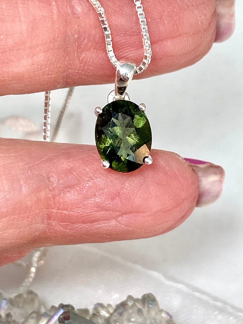 May include: A silver chain necklace with a green gemstone pendant. The gemstone is oval shaped and has a faceted cut.