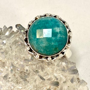 K&ouml;nnte beinhalten: Ein silberner Ring mit einem gro&szlig;en, runden, blaugr&uuml;nen Edelstein, der in einer silbernen Fassung sitzt. Der Ring ist von einem dekorativen silbernen Band mit kleinen Perlen umgeben.