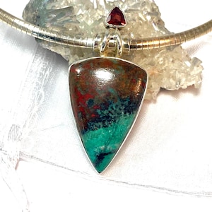 May include: A silver omega chain necklace featuring a large, triangular pendant with a polished, multi-colored stone displaying swirls of deep red, brown, and vibrant turquoise. A small, triangular red gemstone is set above the main pendant.