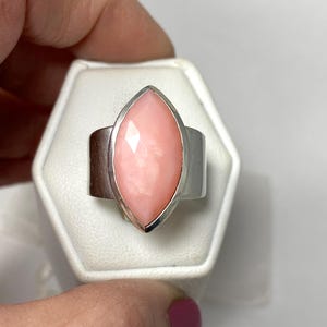 Pode incluir: Um anel de prata com uma gema de opala rosa em forma de marquise.
