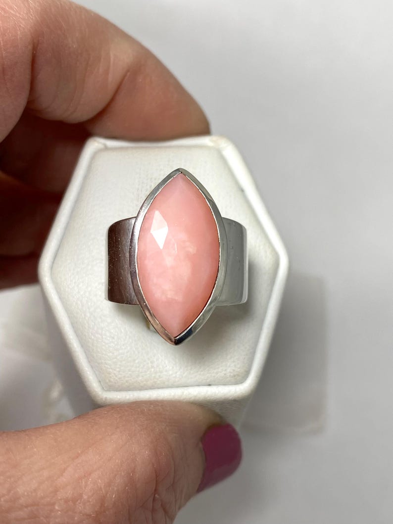 Pode incluir: Um anel de prata com uma gema de opala rosa em forma de marquise.