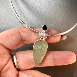 May include: A silver chain necklace with a green and silver pendant. The pendant is a teardrop shape with a black gemstone at the top.