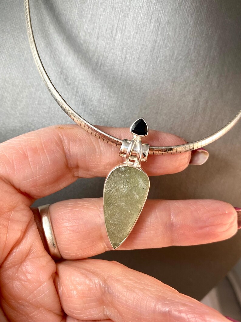 May include: A silver chain necklace with a green and silver pendant. The pendant is a teardrop shape with a black gemstone at the top.