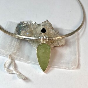 May include: A silver chain necklace with a teardrop-shaped pendant featuring a green stone and a black triangular stone at the top.